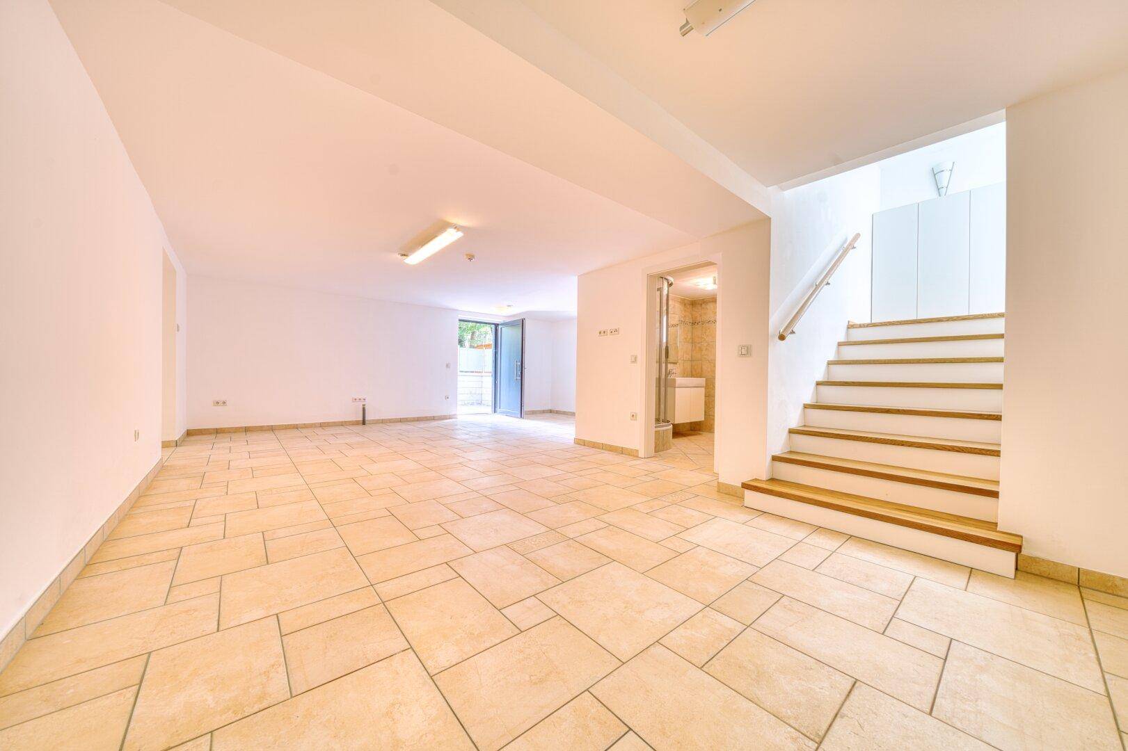 Geräumiger, heller Raum mit Fliesenboden, Treppe und Ausgang ins Freie.