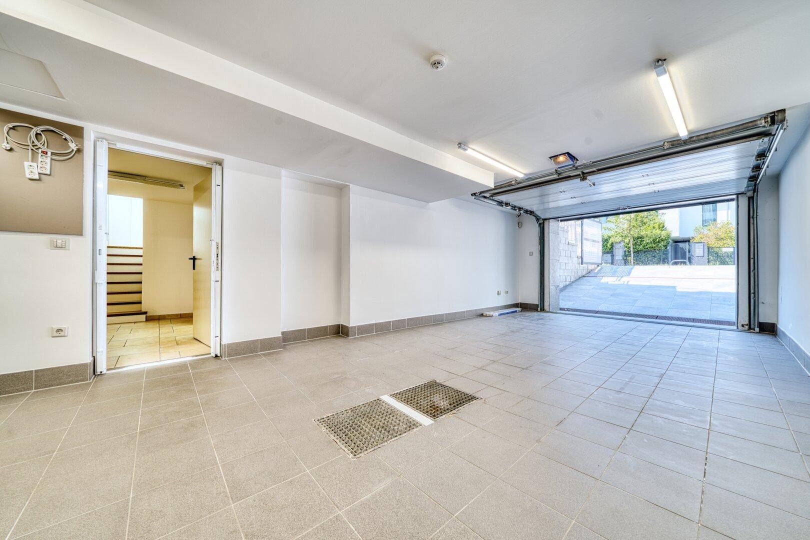 Geräumige Garage mit Fliesenboden, offenem Tor und internem Zugang zum Haus.