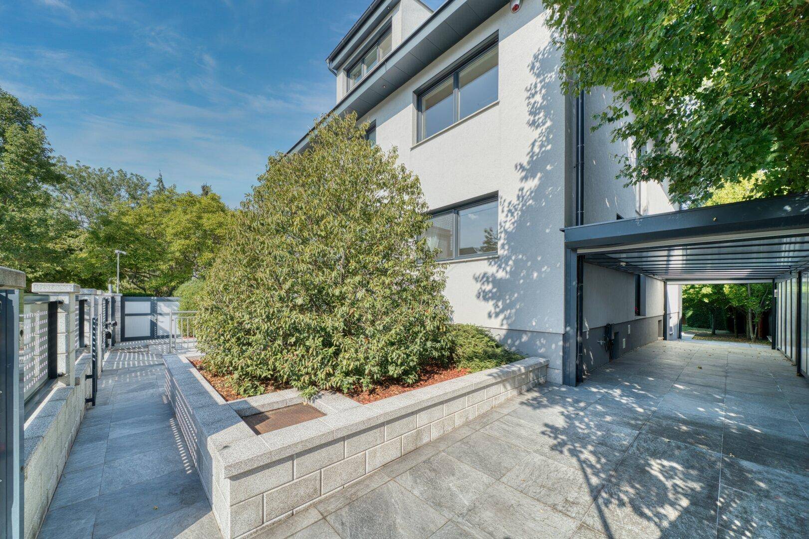 Moderne Gebäudefassade mit gepflastertem Bereich und überdachtem Carport.