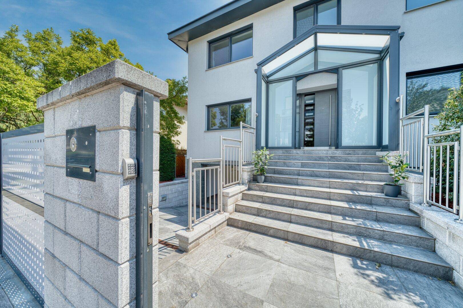 Eingangsbereich eines modernen Hauses mit breiter Treppe und Glasvordach.