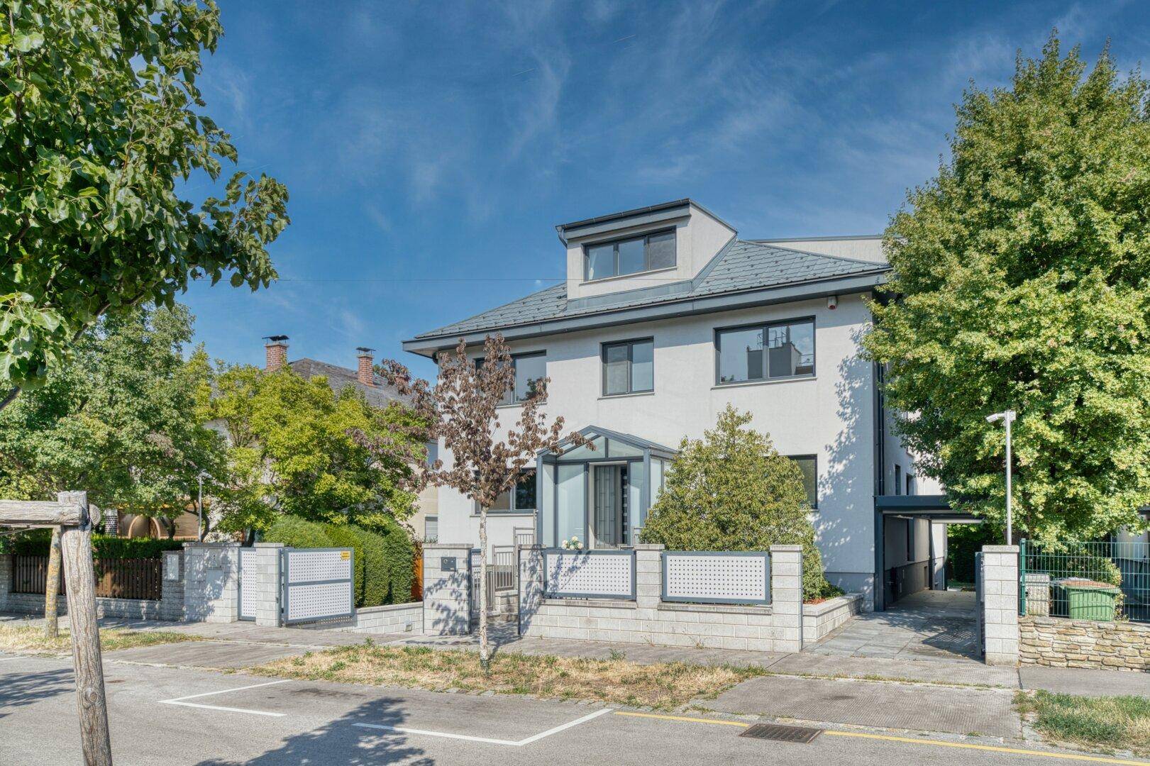 Ansicht eines modernen Einfamilienhauses mit gepflegtem Vorgarten und Zaun.