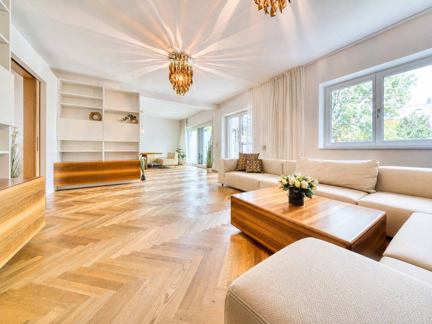 Elegantes Wohnzimmer mit Fischgrätparkett, beigen Sofas und dekorativer Deckenleuchte.