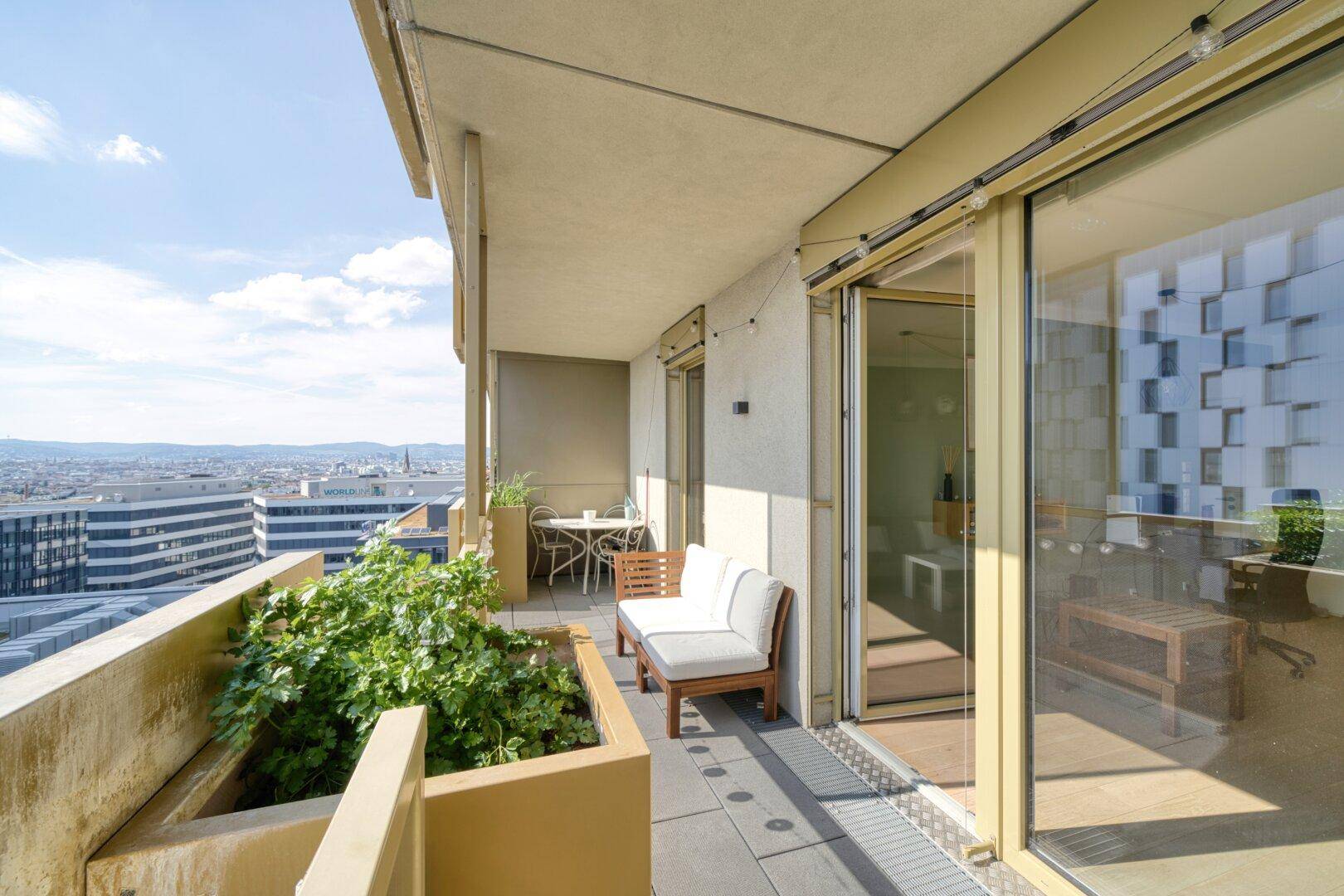 Geräumiger Balkon mit Sitzgelegenheiten und Pflanzen, der einen weiten Blick über die Stadt bietet.