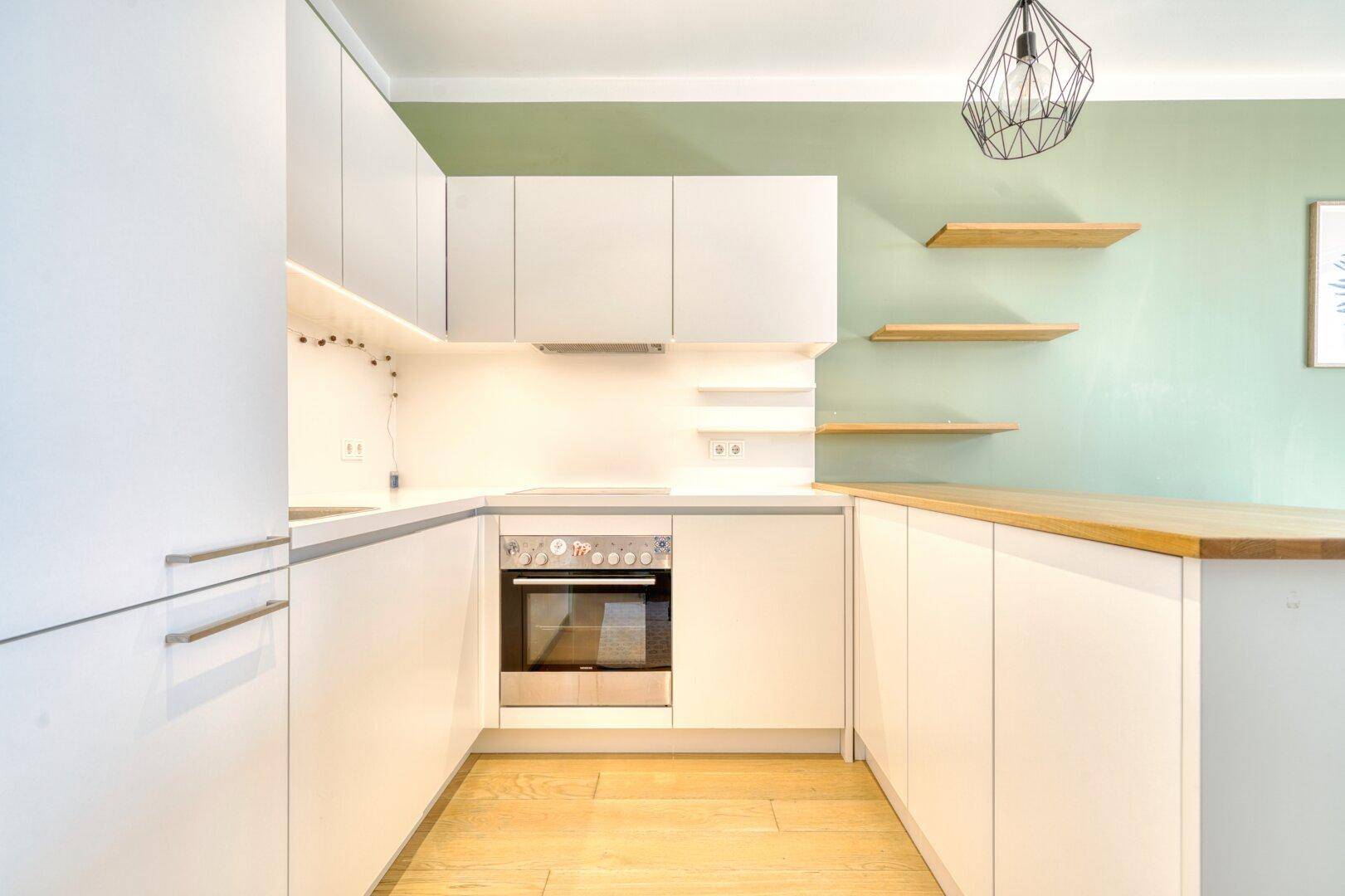Moderne Einbauküche mit weißen Schränken, integriertem Backofen und heller Holz-Arbeitsplatte.