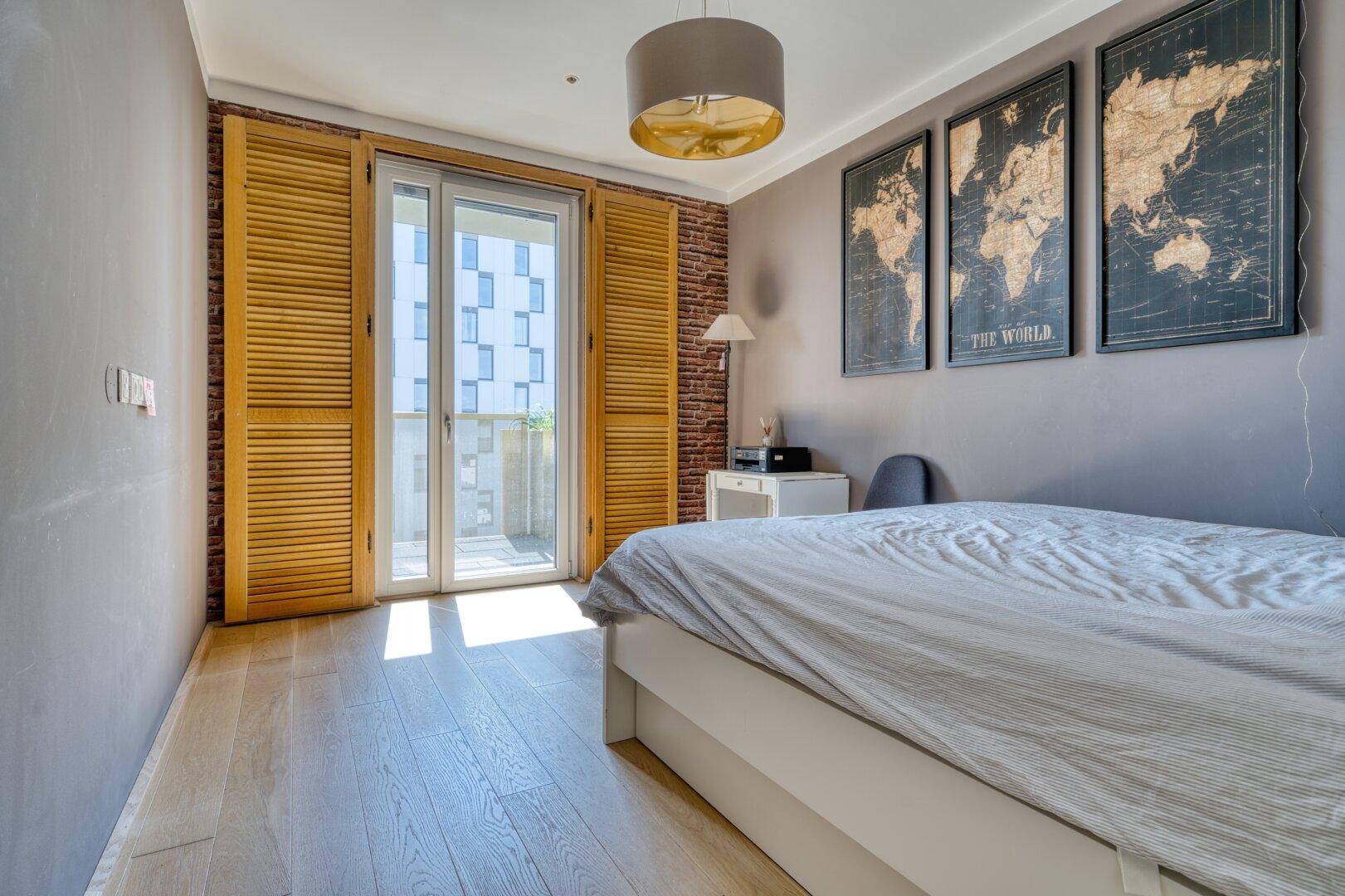 Schlafzimmer mit Holzboden, Akzentwand aus Ziegeln und Zugang zu einem Balkon mit Holzläden.