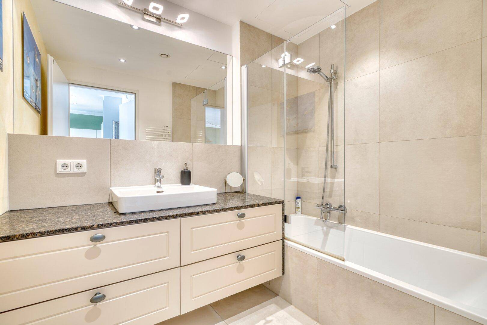 Modernes Badezimmer mit Badewanne, Duschabtrennung, Einzelwaschbecken und hellen Fliesen.