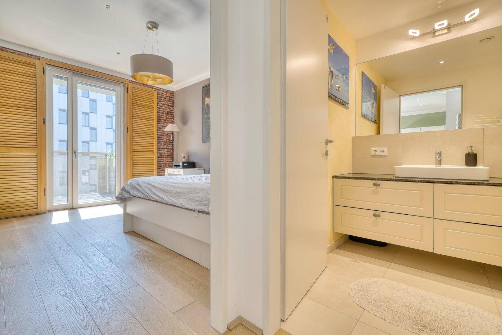 Schlafzimmer mit Holzboden und direktem Zugang zu einem modernen Badezimmer.