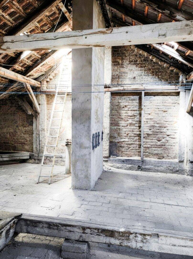 Unausgebauter Dachboden mit sichtbaren Holzbalken, Ziegelwänden und einer Leiter, bereit für die Renovierung.