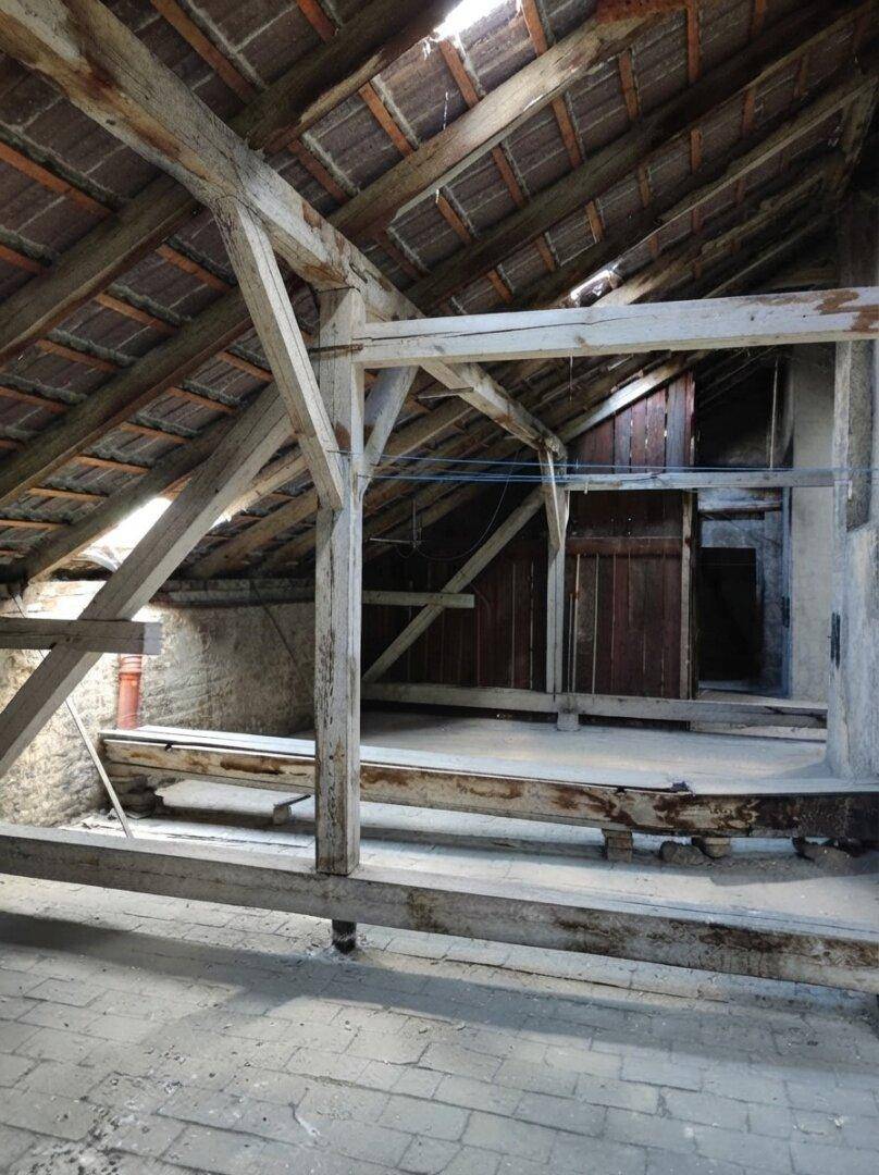Dachboden mit Blick auf ein Fenster und die rohe Holzkonstruktion des Daches, lichtdurchflutet.