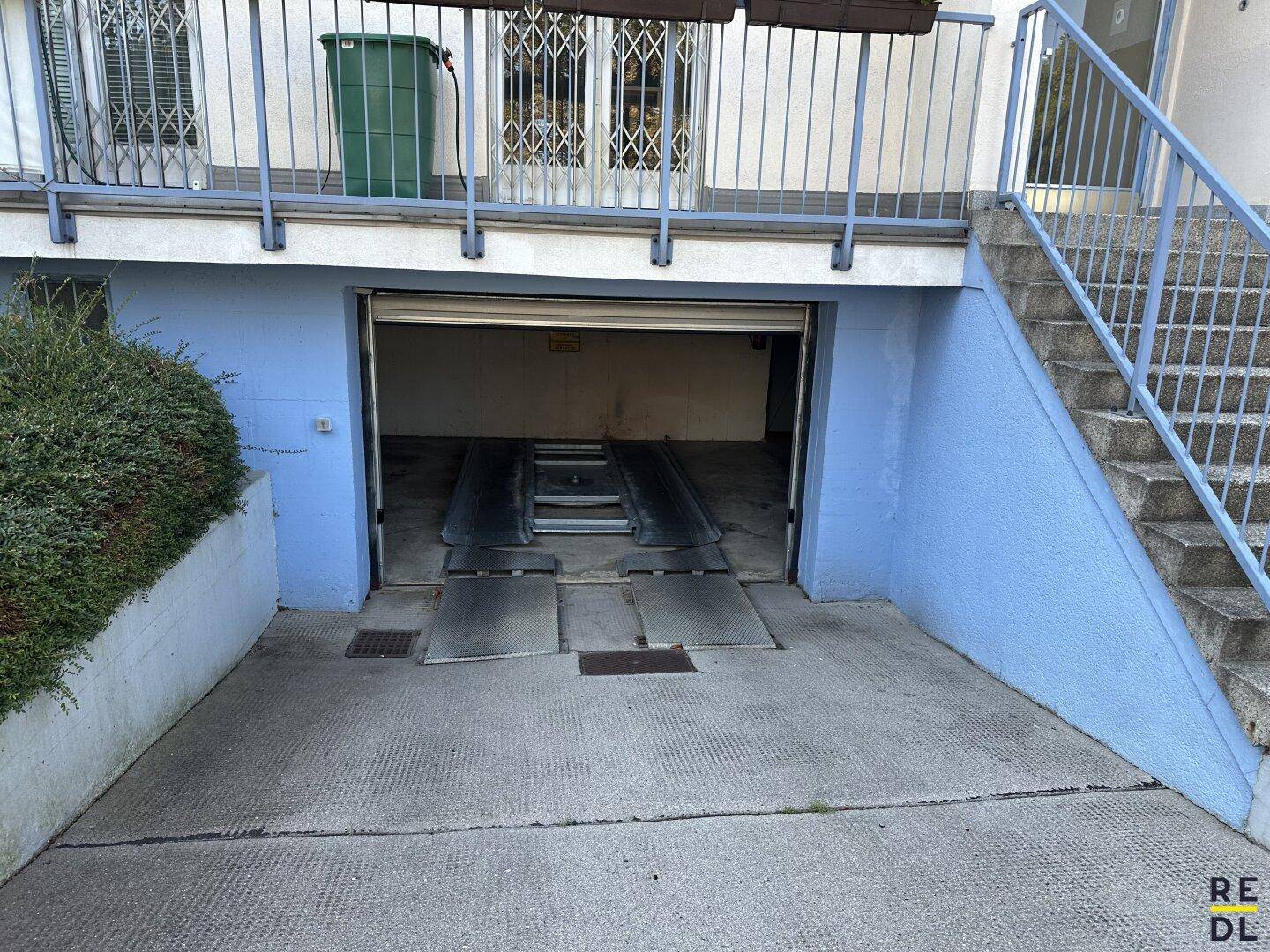 Offener Eingang zur Tiefgarage mit sichtbarem Autoaufzug und Zufahrtsrampe.