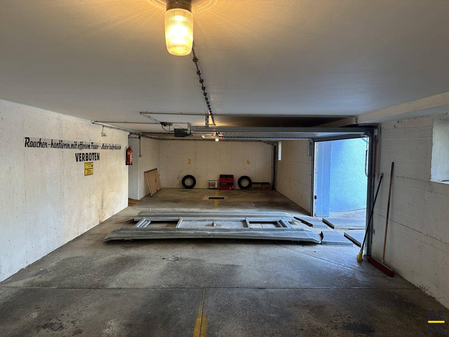 Geräumige Tiefgarage mit Autoaufzug, Beleuchtung und Hinweisschildern an den Wänden.