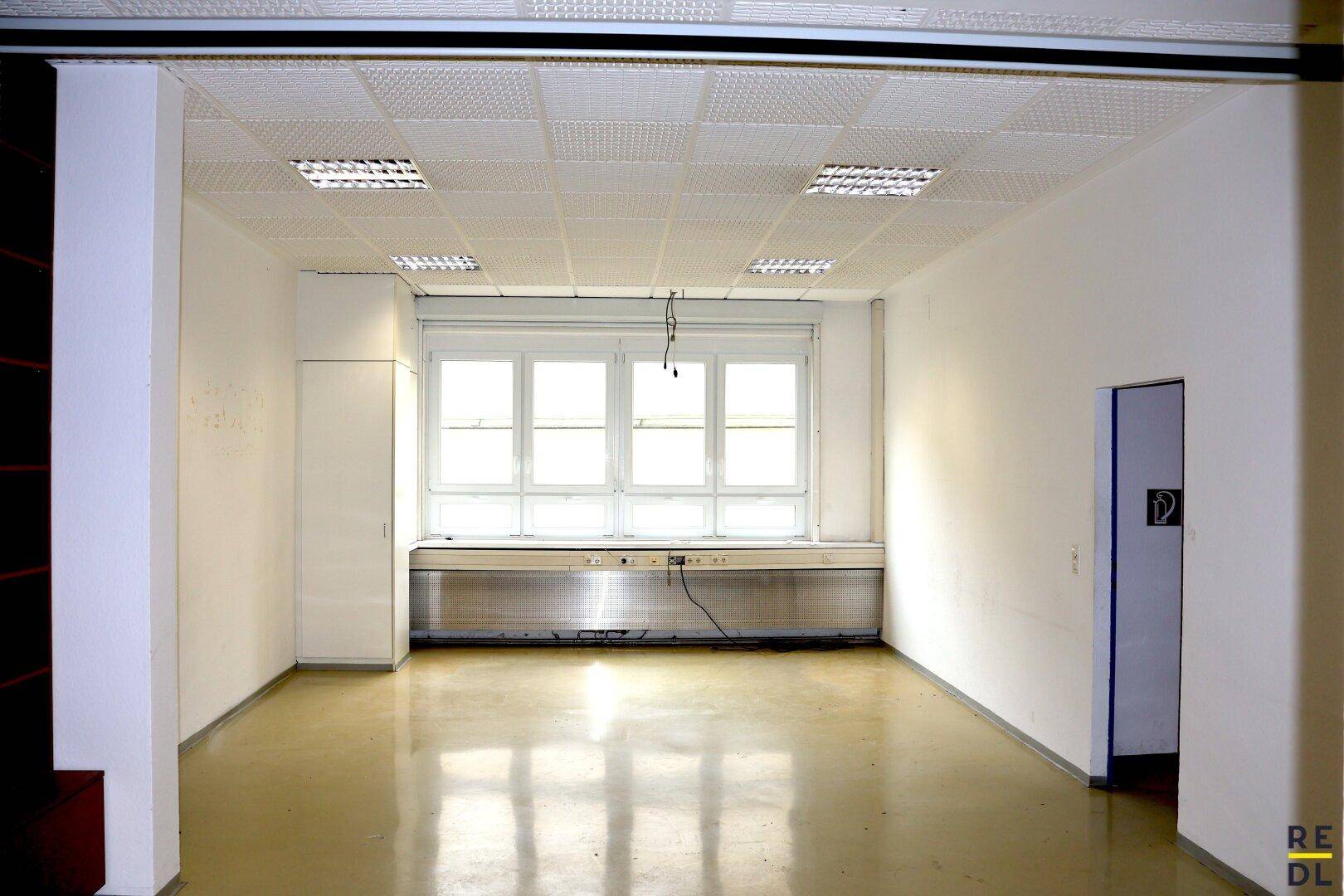 Leerer Büroraum mit großer Fensterfront, abgehängter Decke und integrierter Beleuchtung.