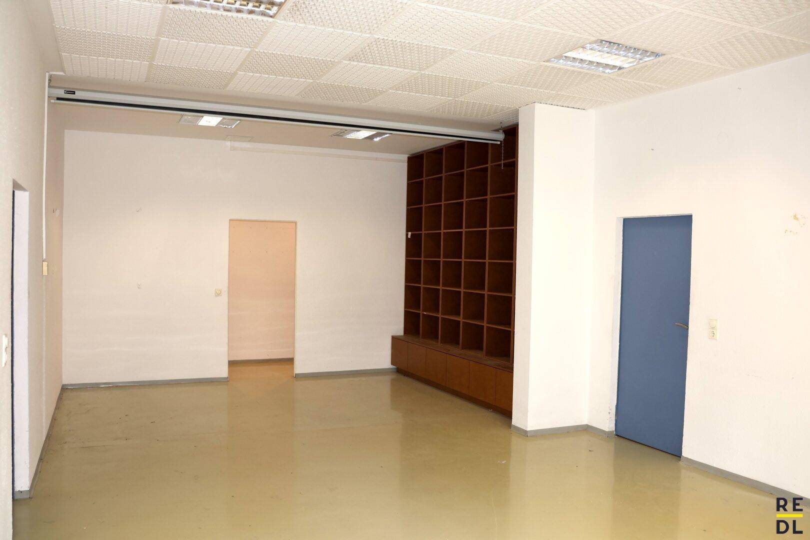Leerer Büroraum mit eingebautem Holzregal und abgehängter Decke.