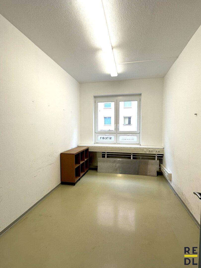 Kleiner, heller Büroraum mit einem Fenster und einem niedrigen Holzregal.