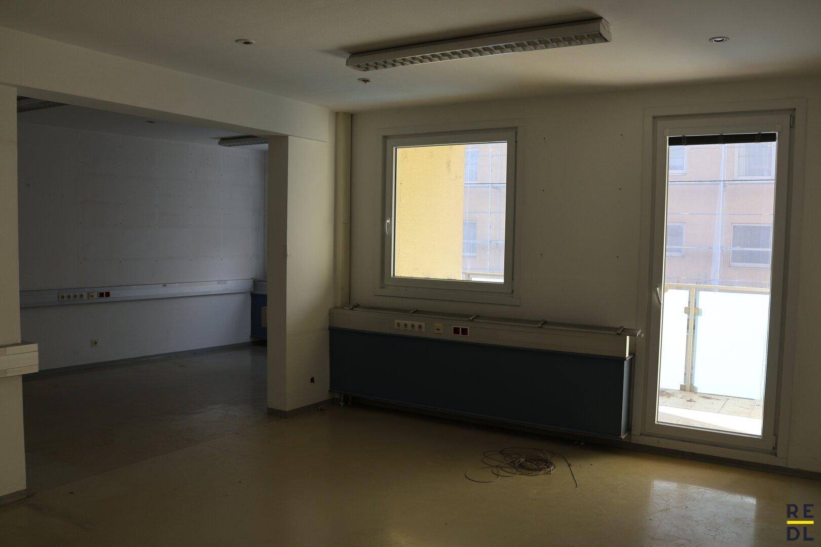 Leerer Raum mit großem Fenster und Zugang zu einem kleinen Balkon, ideal als Bürofläche.