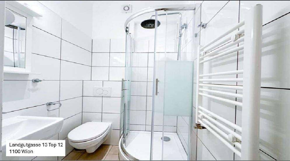Helles Badezimmer mit weiß gefliesten Wänden, Duschkabine und beheiztem Handtuchhalter.