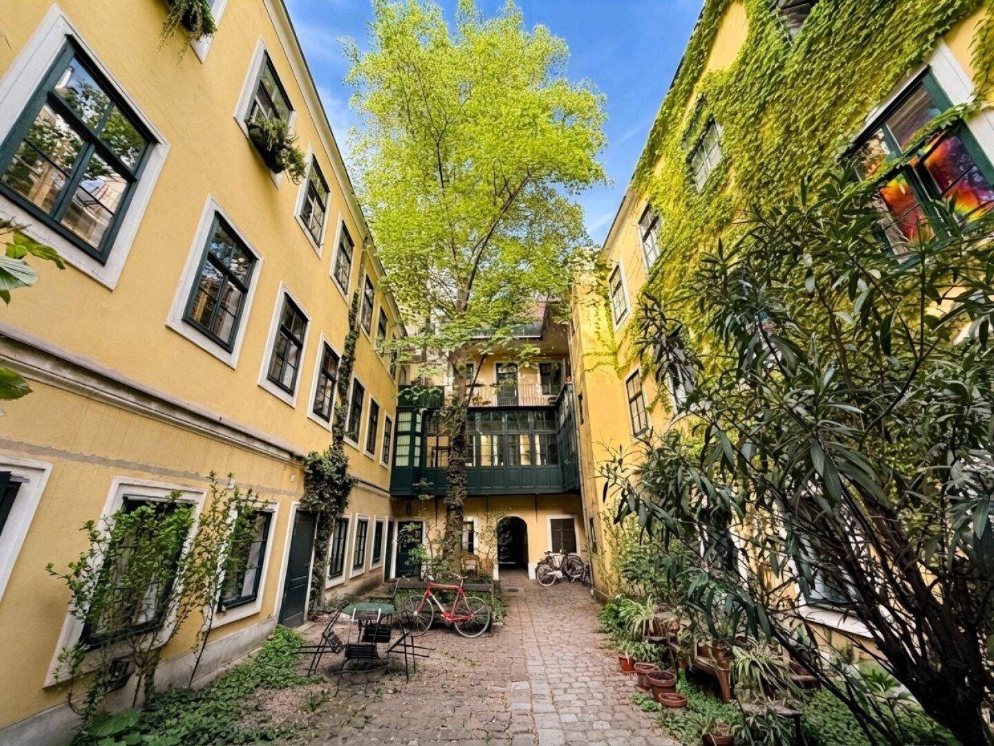 Malerischer Innenhof mit gelben Fassaden, viel Grün und einem kleinen Sitzbereich.