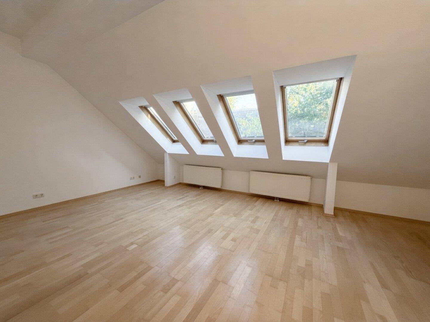Heller Dachbodenraum mit schrägen Wänden, Holzboden und einer Reihe von vier Dachfenstern.