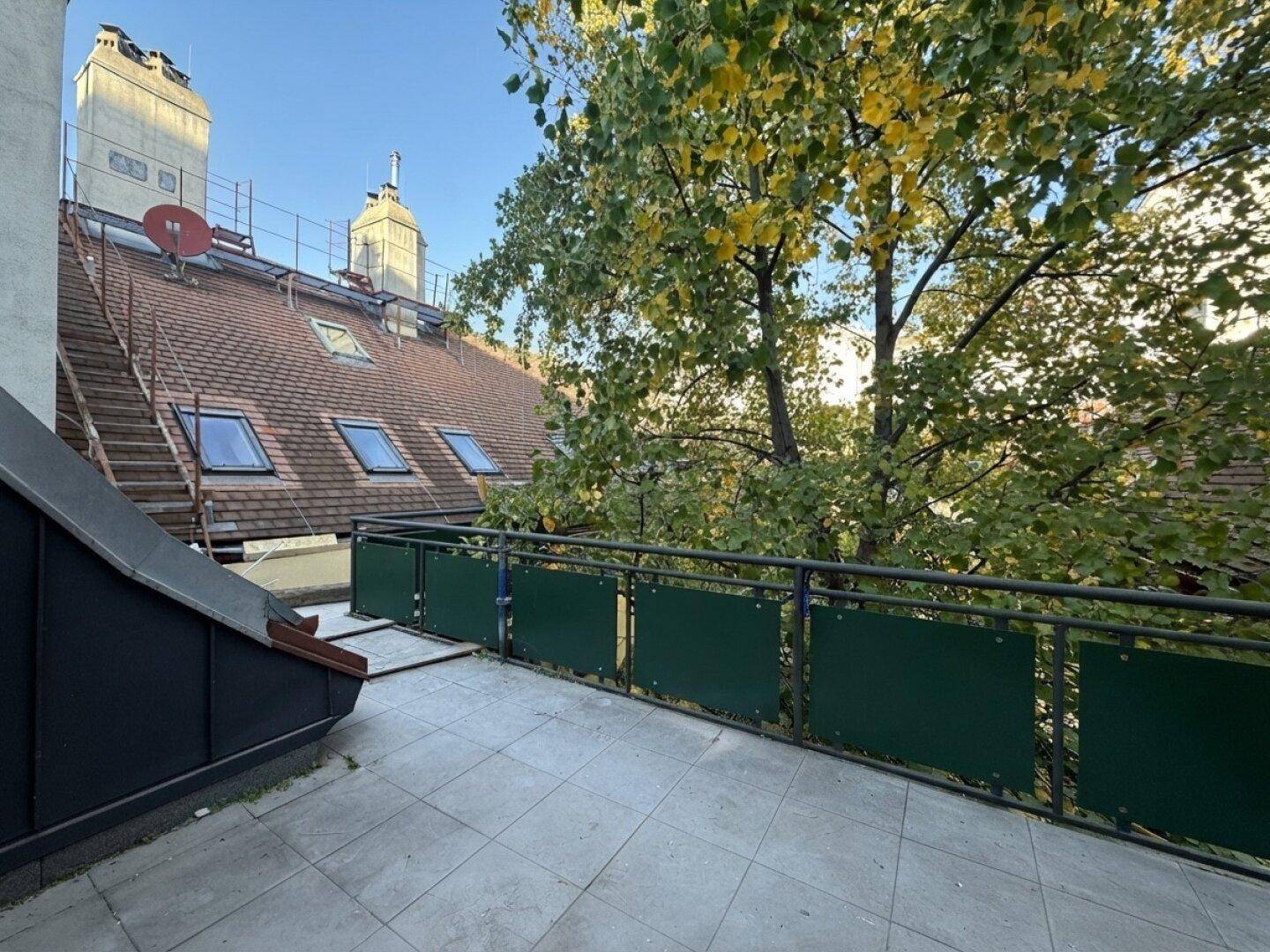 Balkon mit Fliesenboden und Blick auf die umliegenden Dächer und Bäume.