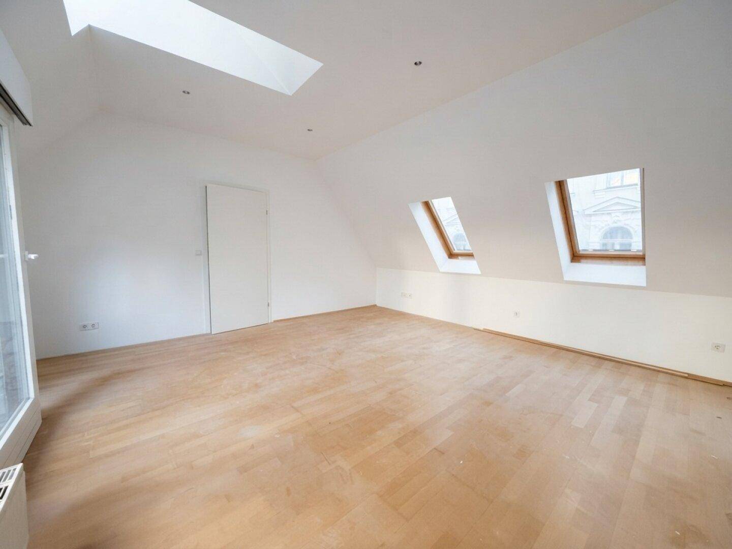 Geräumiges Dachgeschosszimmer mit hellen Holzböden und mehreren Dachfenstern für viel Licht.