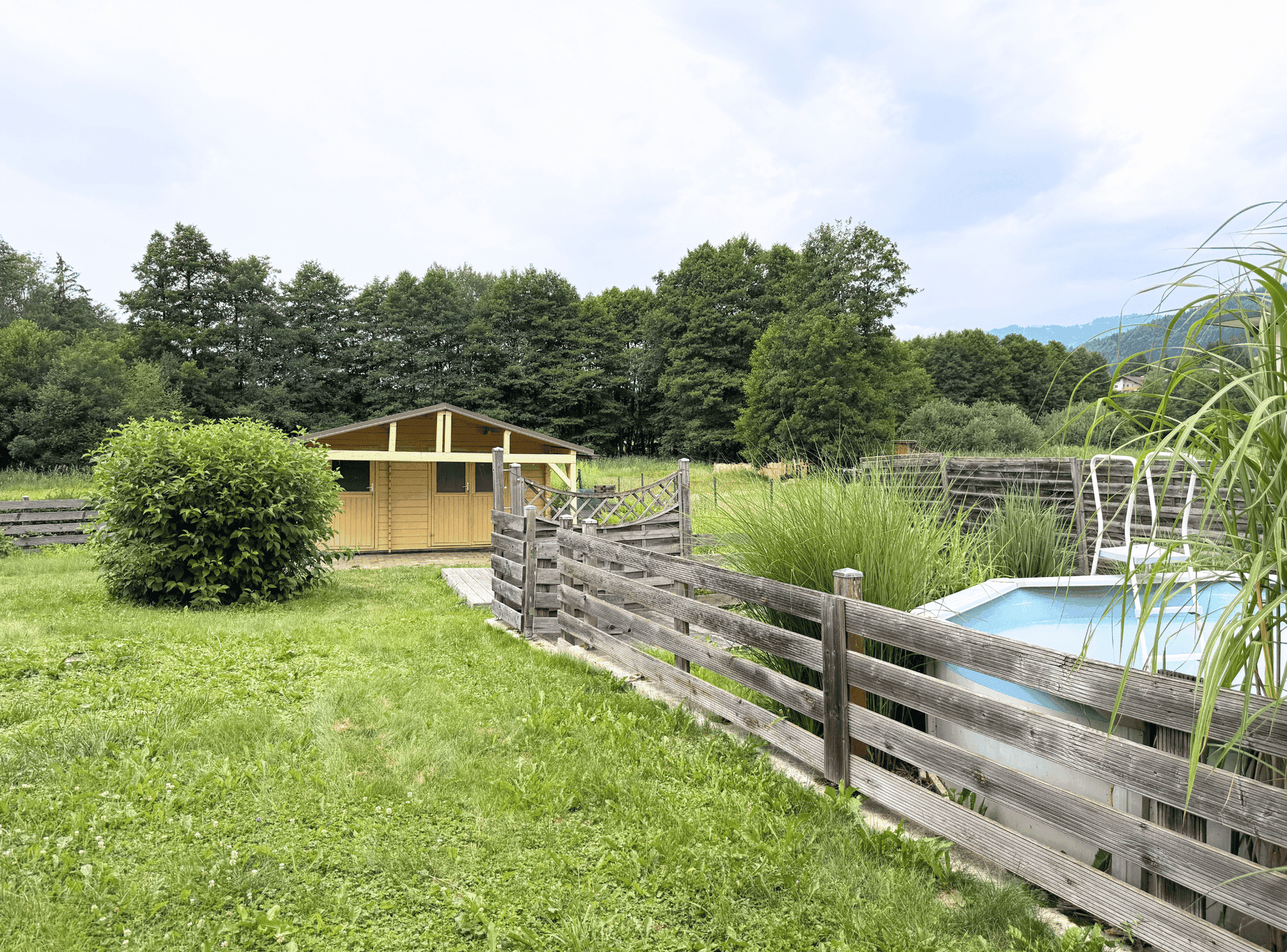 Weitläufiger Gartenbereich mit Holzschuppen, kleinem Pool und Blick ins Grüne.