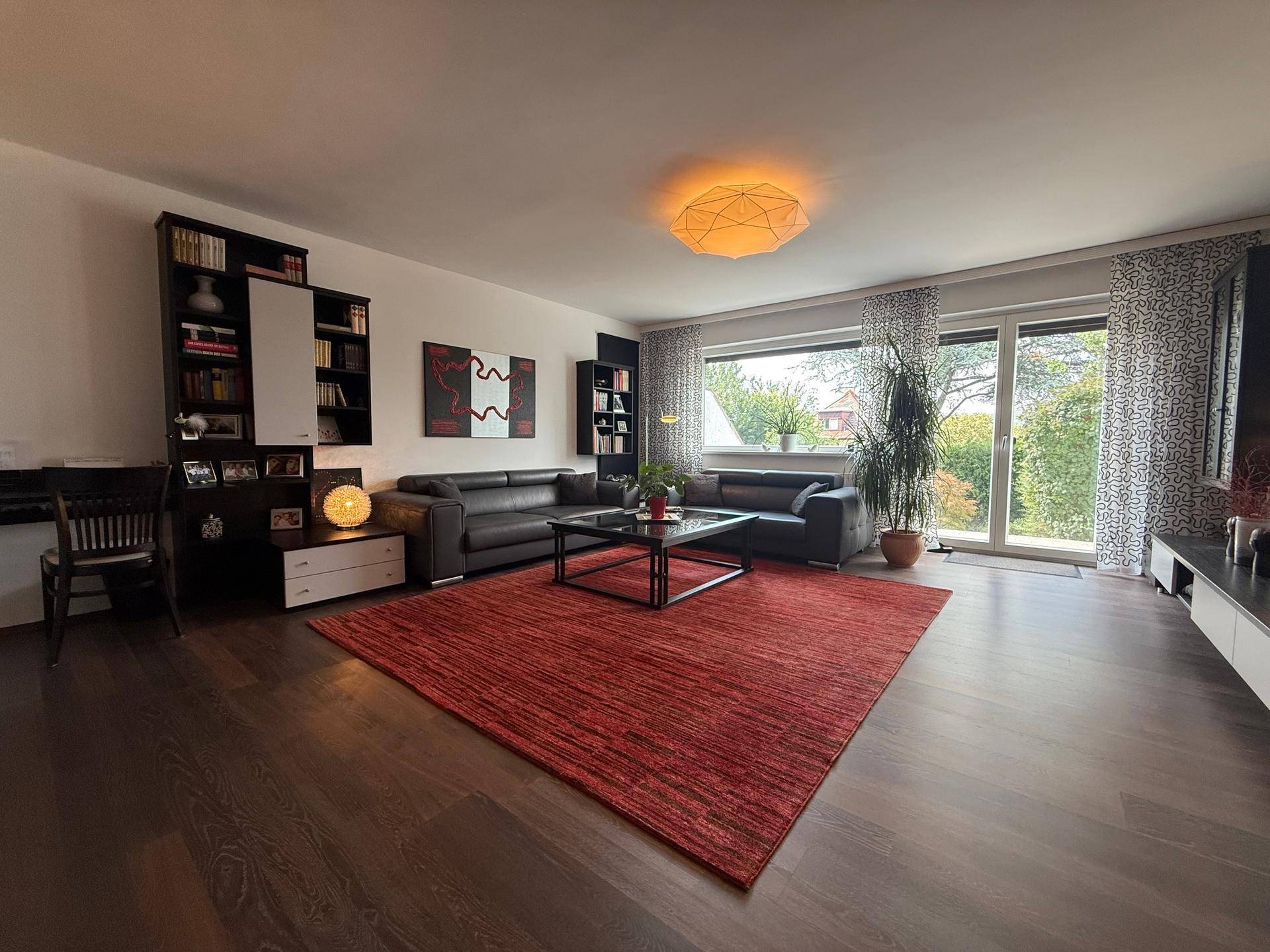 Geräumiges Wohnzimmer mit dunklem Holzboden, bequemen Sofas und einem großen roten Teppich.