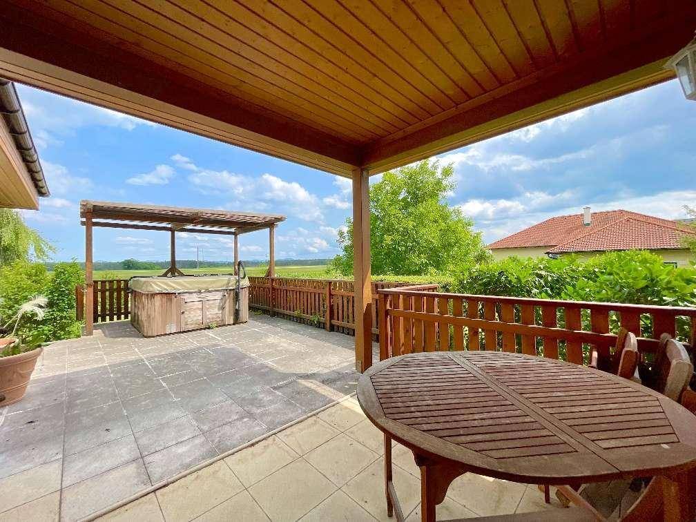 Überdachte Terrasse mit Holzboden, Sitzgelegenheiten und einem Whirlpool im Freien.