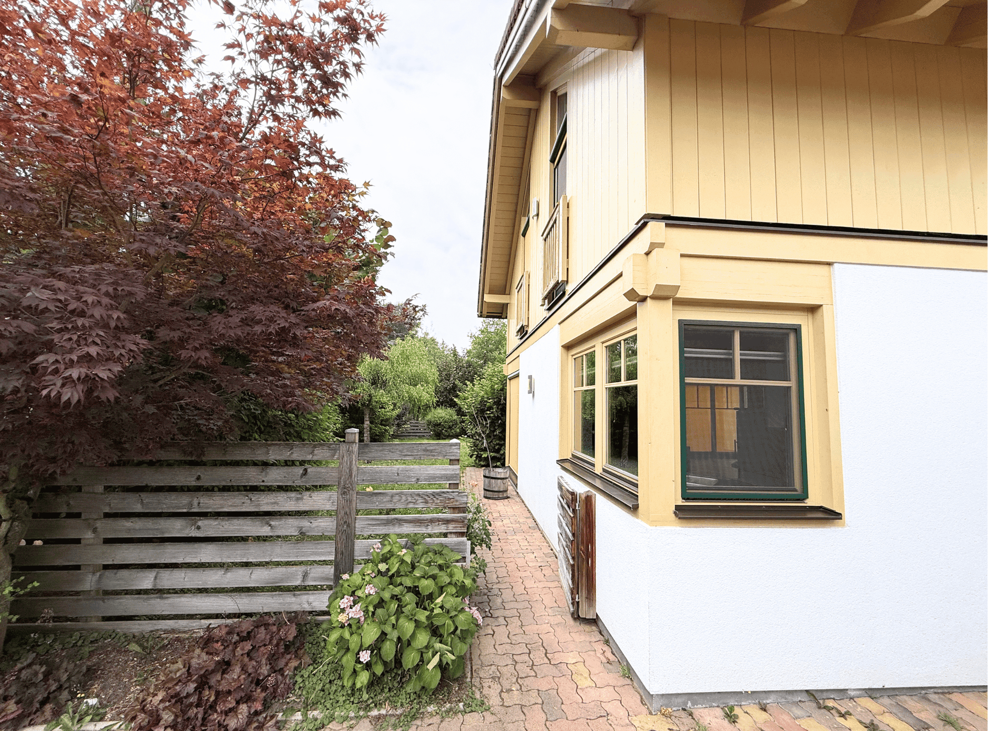 Seitenansicht des Hauses mit gepflastertem Weg und üppiger Bepflanzung.