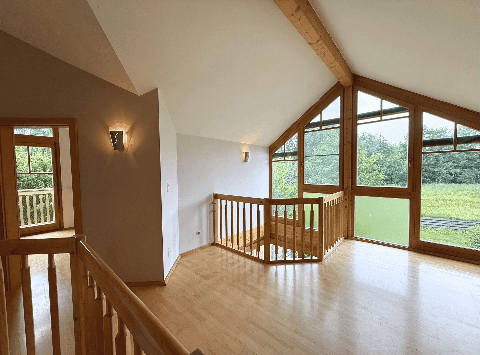 Helle Galerie im Obergeschoss mit Holzboden, sichtbaren Balken und großen Fenstern.
