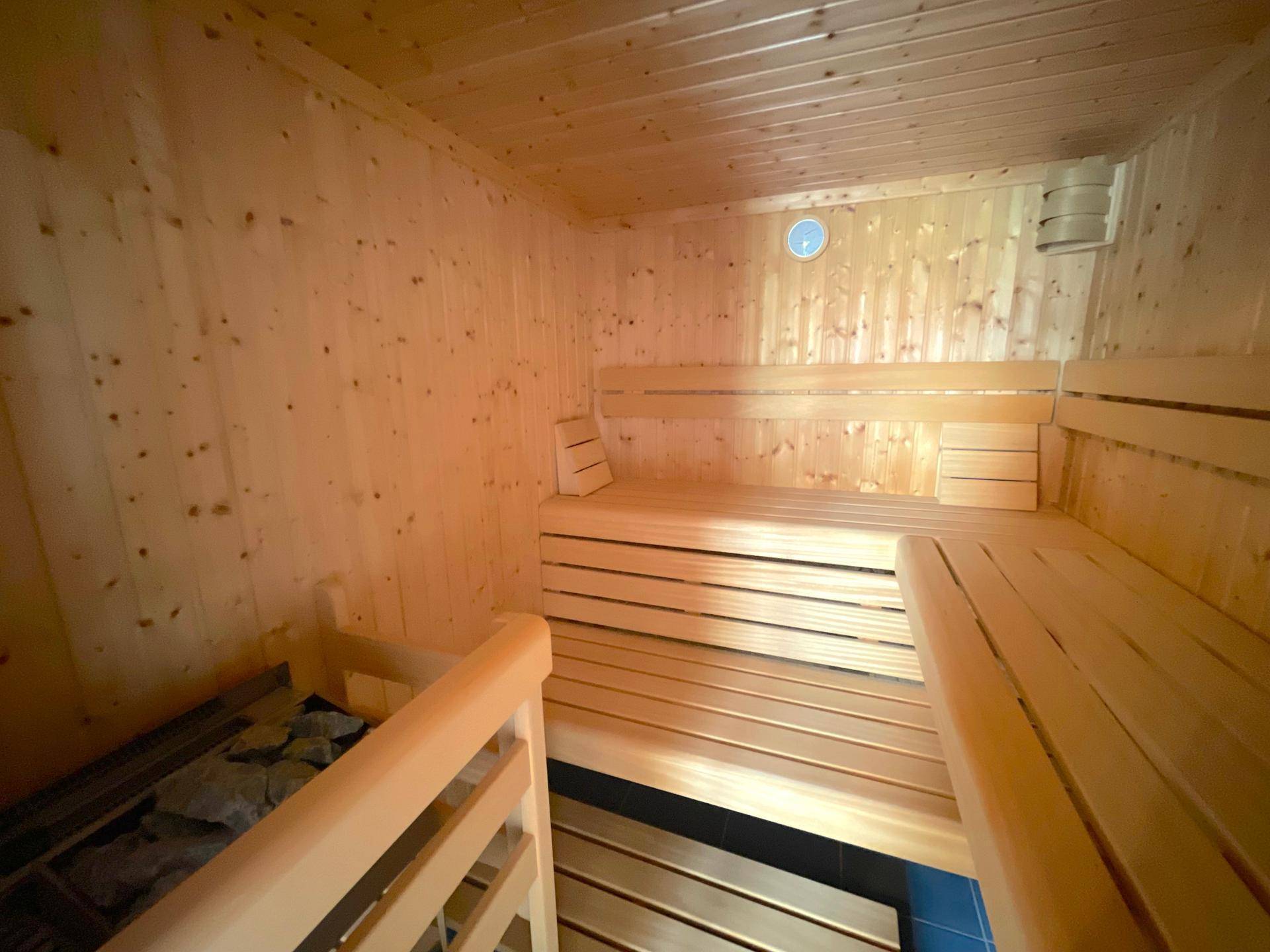 Innenansicht einer holzvertäfelten Sauna mit mehreren Sitzebenen und Heizofen.