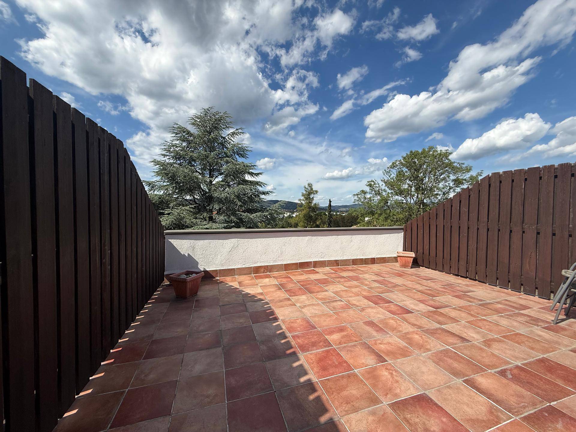 Geräumige Terrasse mit Terrakotta-Fliesen und Holzzäunen, bietet viel Platz im Freien.