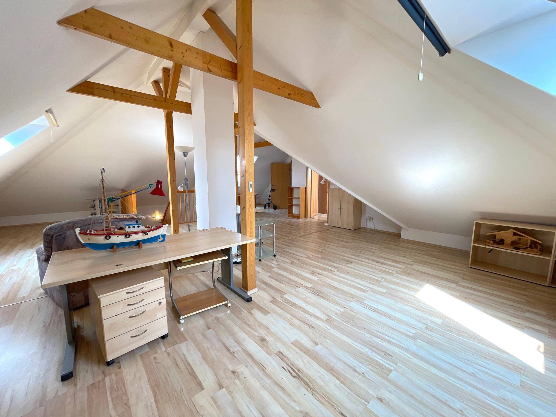 Helles Dachgeschoss mit sichtbaren Holzbalken, Laminatboden und viel natürlichem Licht.
