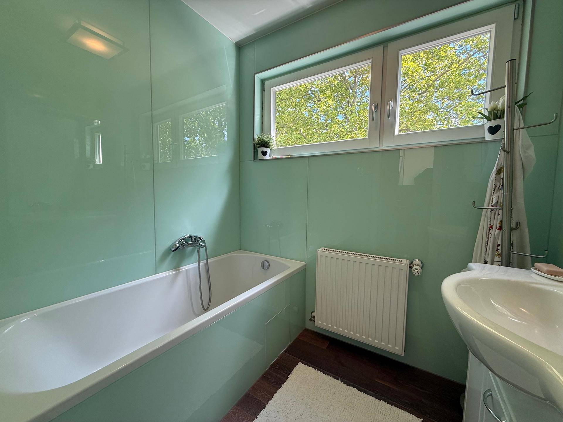 Modernes Badezimmer mit Badewanne, Waschbecken und Fenster, in frischem Mintgrün gehalten.