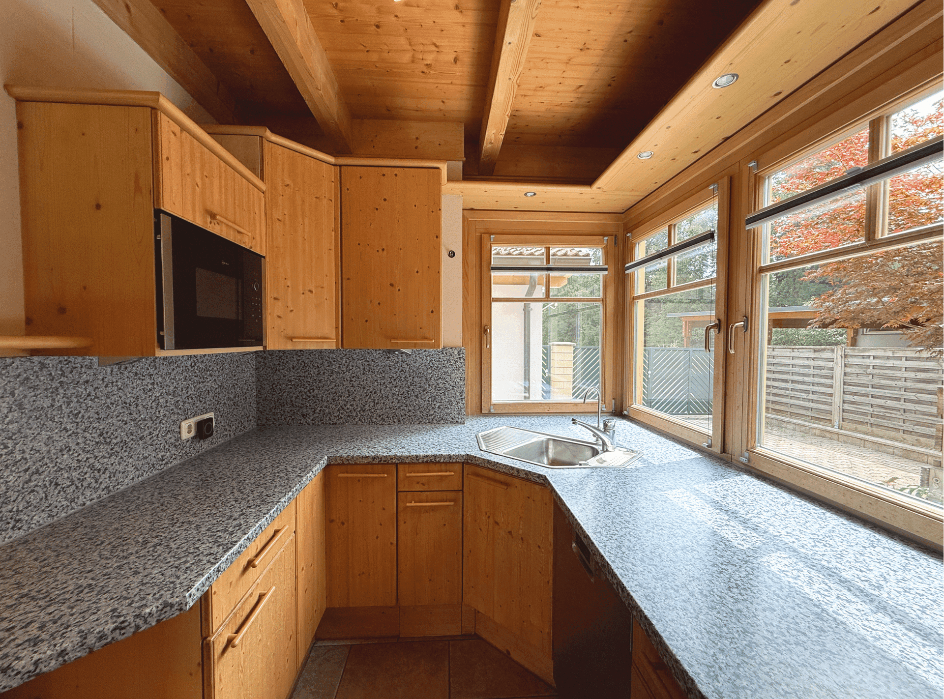 Helle Holzküche mit Granitarbeitsplatten, Spülbecken und Fenster mit Blick nach draußen.