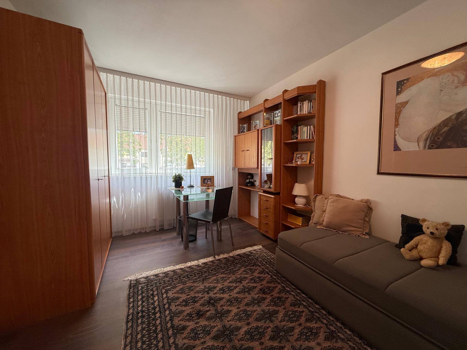 Helles Zimmer mit Schreibtisch, Bücherregal und Schlafsofa, ideal als Gäste- oder Arbeitszimmer.
