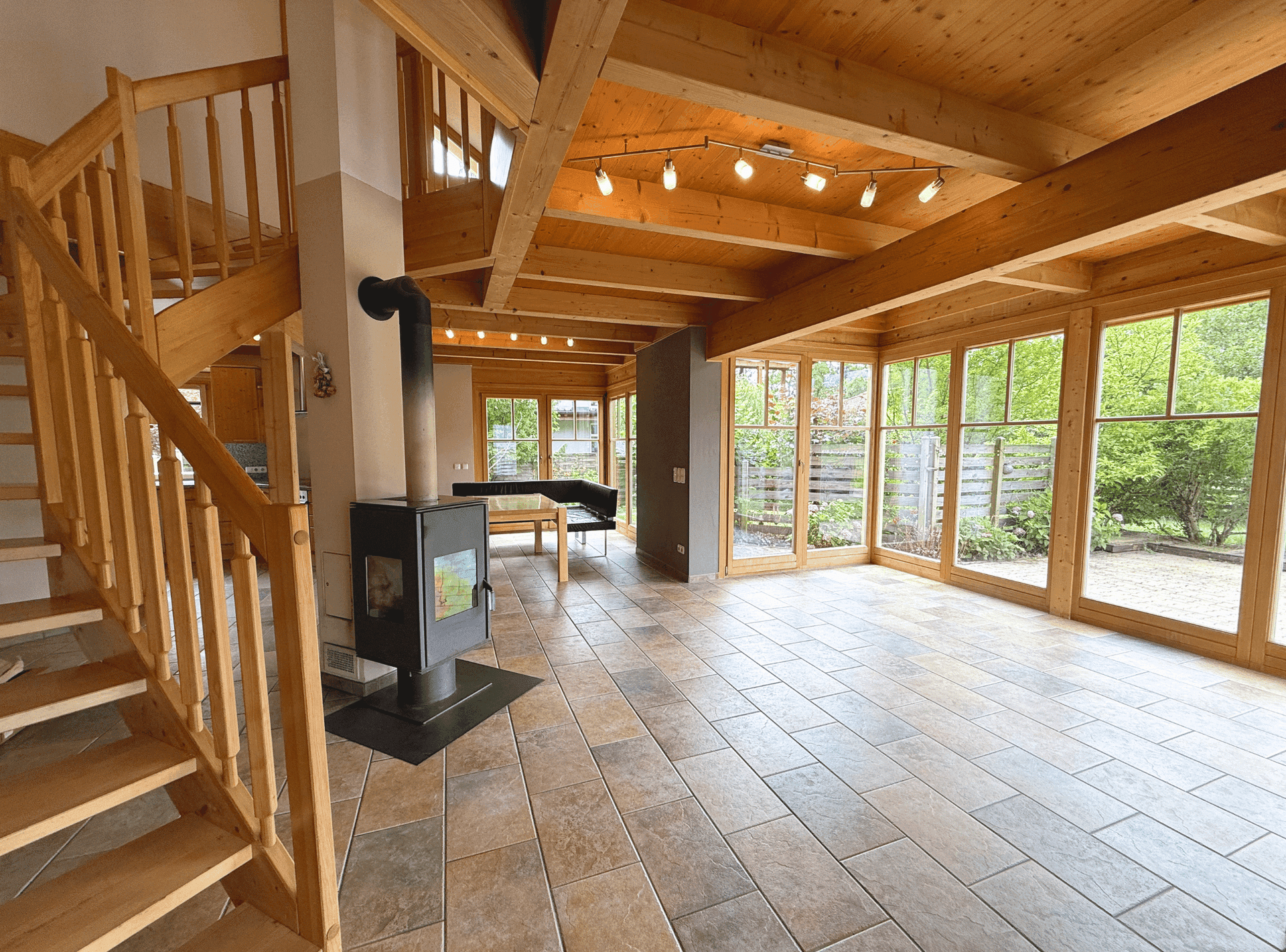 Helles Wohnzimmer mit Holztreppe, Fliesenboden und zentral platziertem Holzofen.