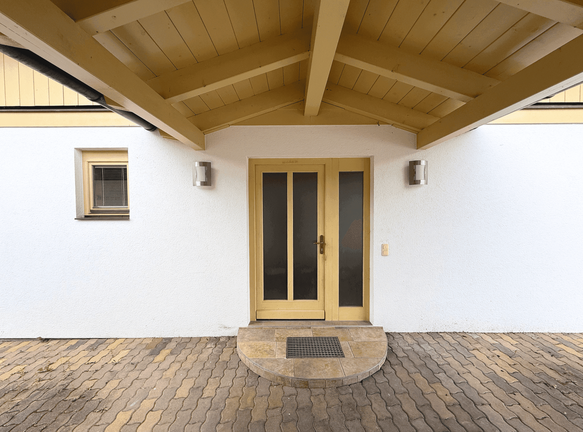 Eingangsbereich des Hauses mit überdachtem Vordach und Holztür.