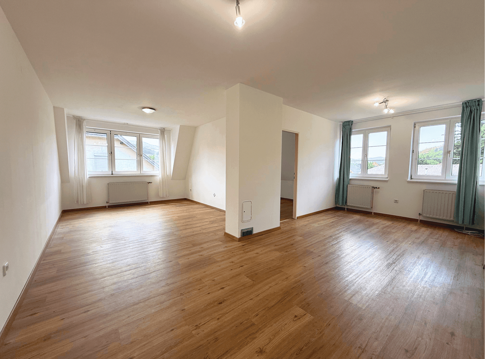 Geräumiger, heller Raum mit Holzfußboden und mehreren Fenstern, bereit zur individuellen Gestaltung.