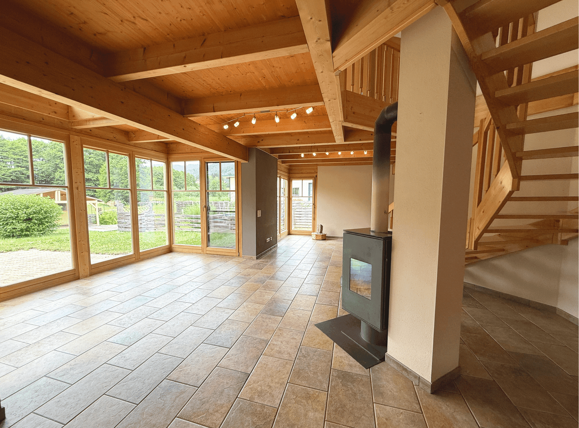 Geräumiges Wohnzimmer mit Fliesenboden, großen Fenstern und gemütlichem Holzofen.