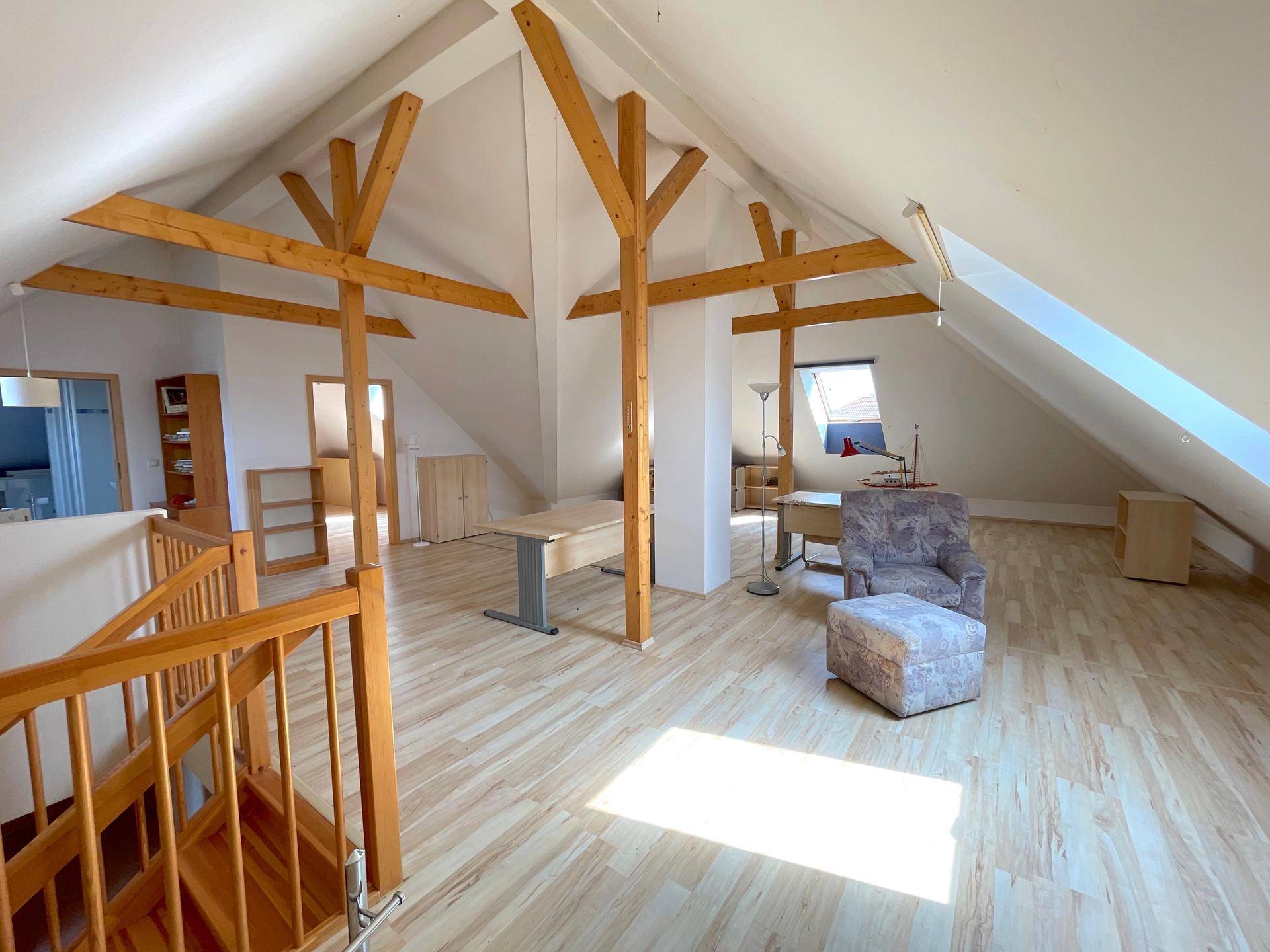 Geräumiges Dachgeschoss mit Holzbalken, Laminatboden und Treppenzugang, ideal als Wohn- oder Arbeitsbereich.