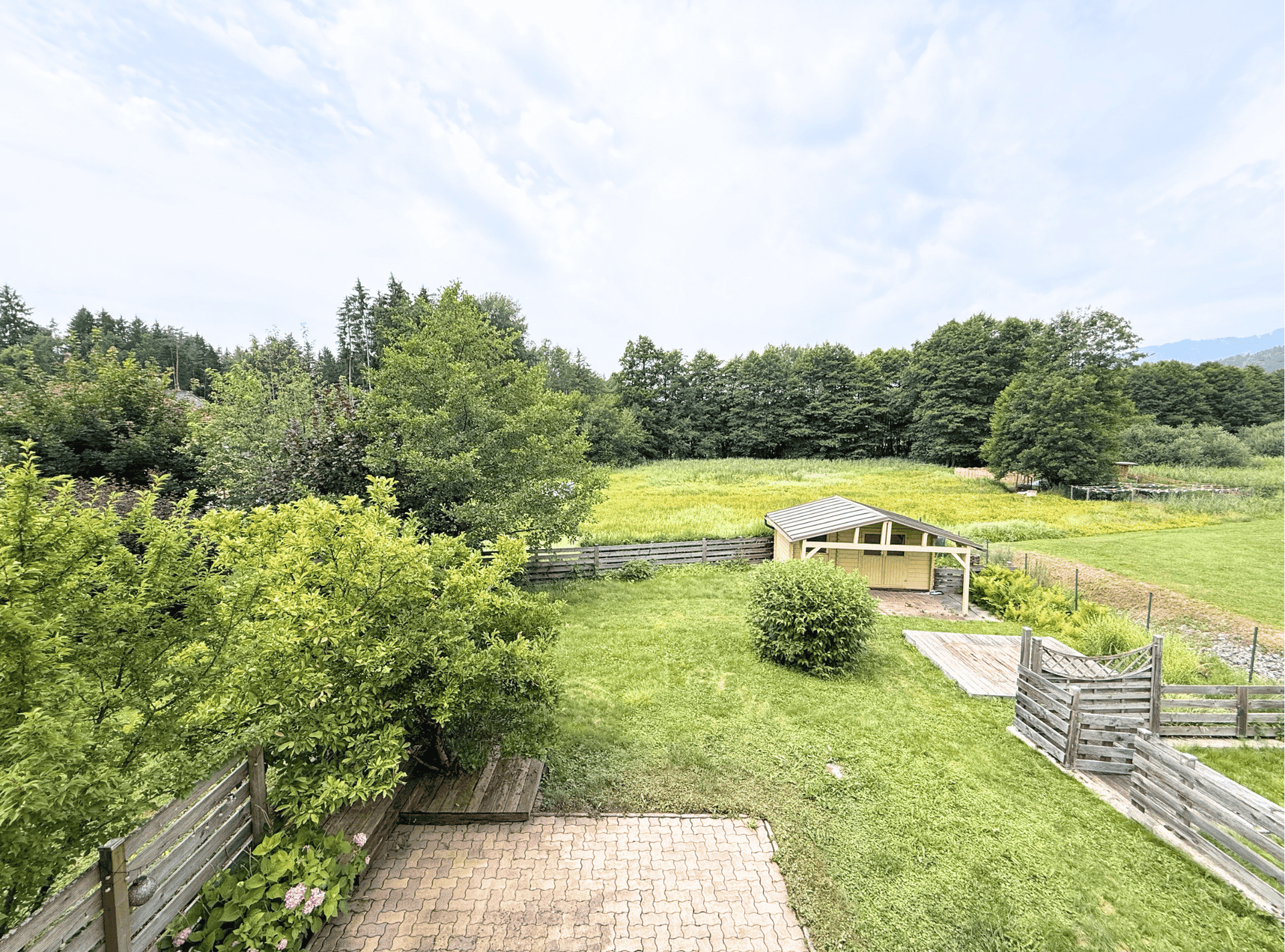 Blick von oben auf den Garten mit Terrasse, Holzschuppen und weitem Blick in die Natur.