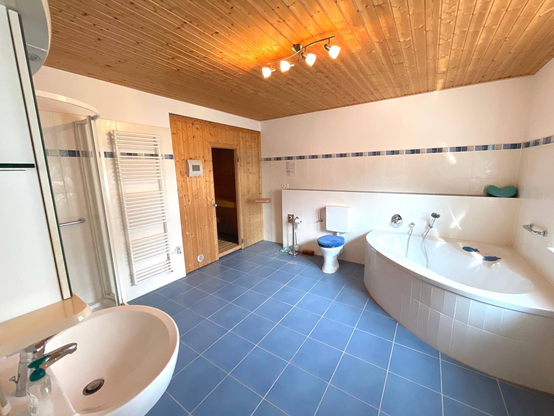 Geräumiges Badezimmer mit blauen Fliesen, Eckbadewanne, Dusche und integrierter Sauna.