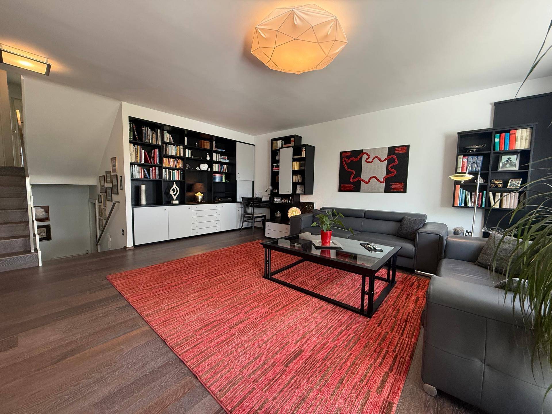 Helles Wohnzimmer mit integrierten Bücherregalen, dunklem Boden und Zugang zur Treppe.