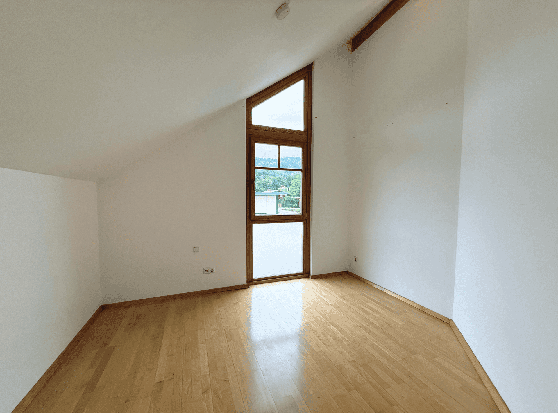 Geräumiges Zimmer im Dachgeschoss mit Holzboden, Dachschräge und Fenster mit Ausblick.