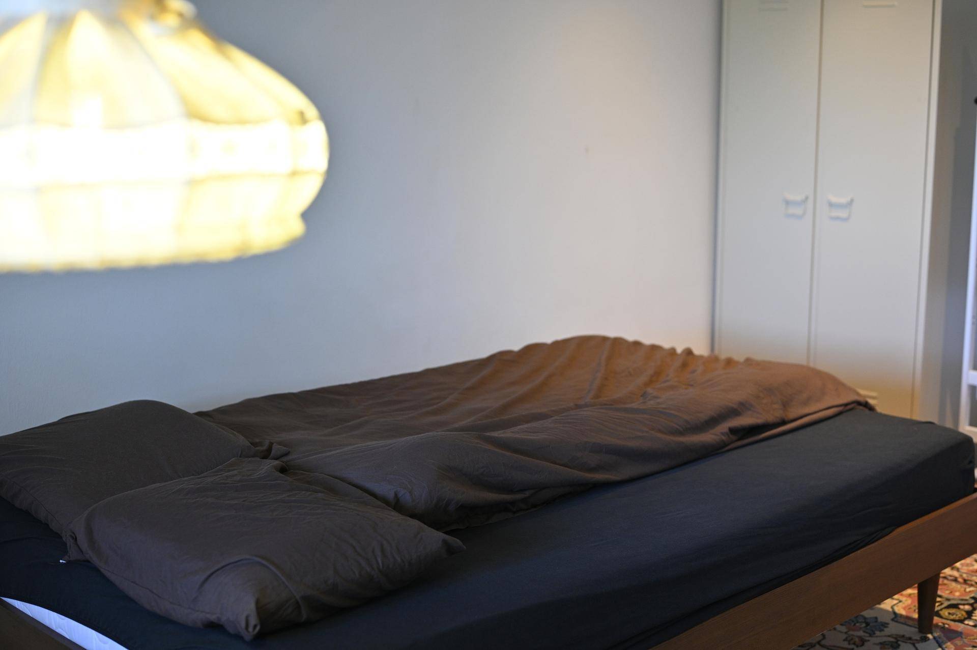 Schlafzimmer mit dunklem Bett und einem weißen Einbauschrank im Hintergrund.