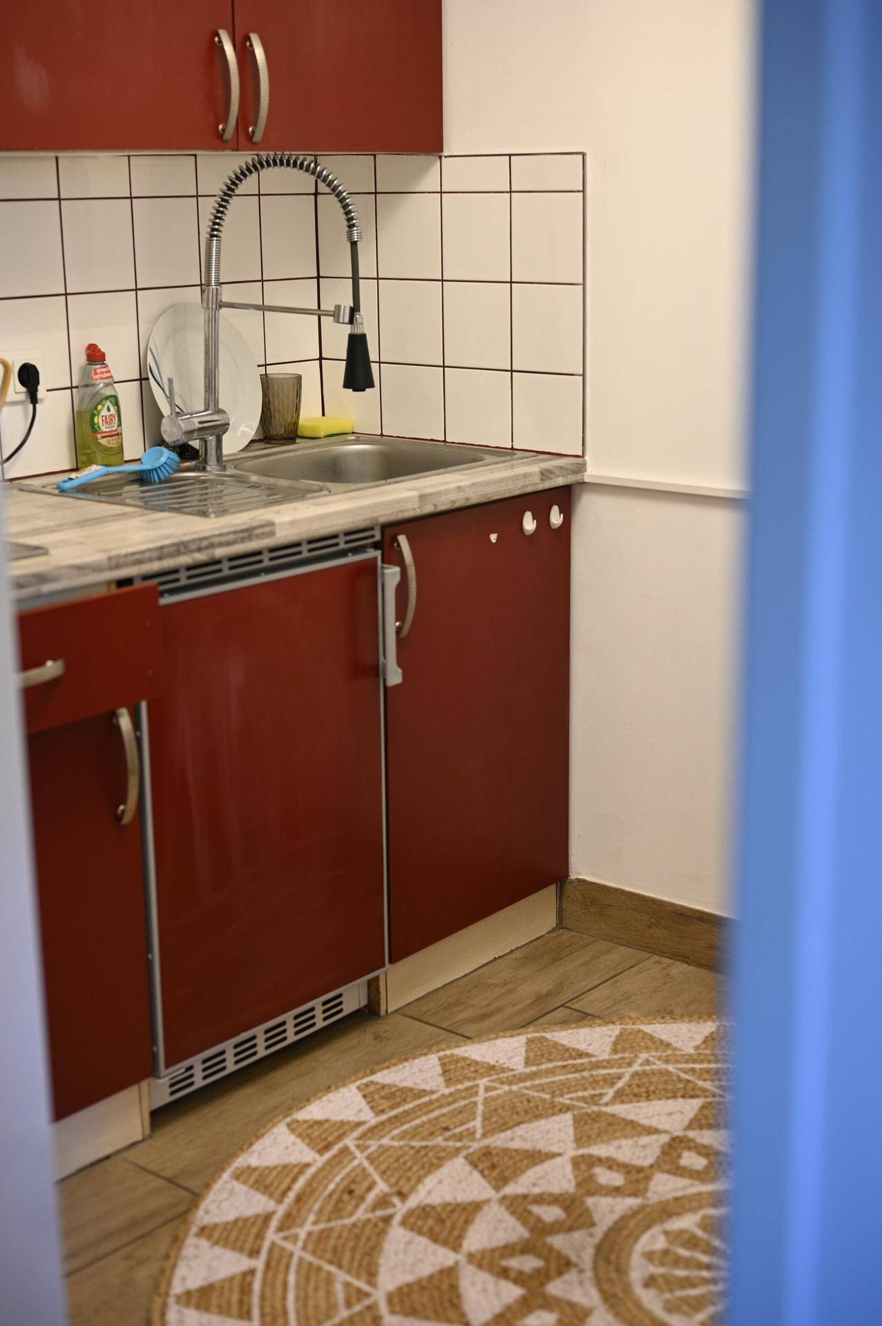Kleine Küchenzeile mit roten Schränken, Spülbecken und einem runden Teppich auf dem Boden.