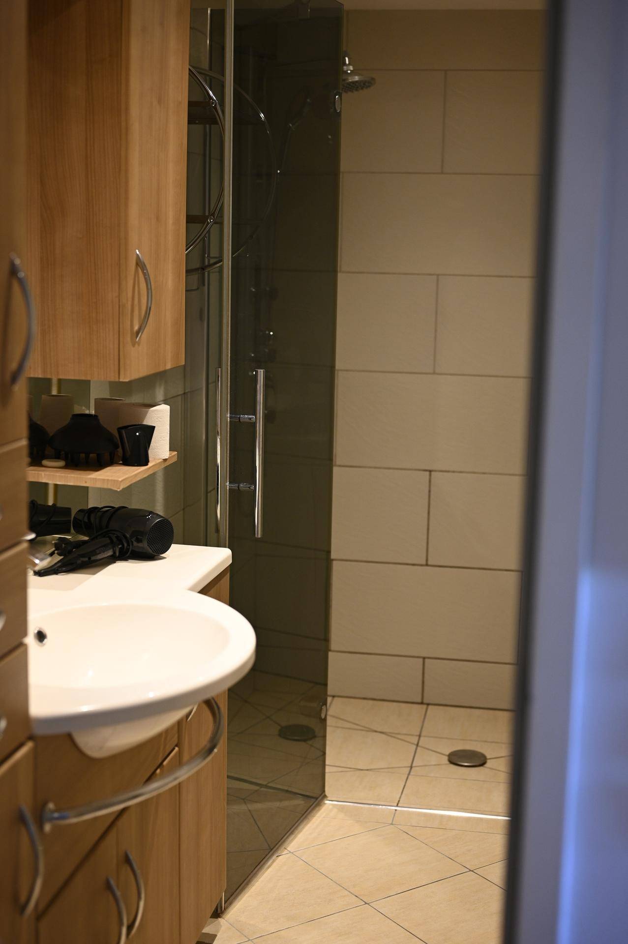 Modernes Badezimmer mit Holzschränken, Waschbecken und einer begehbaren Duschkabine aus Glas.