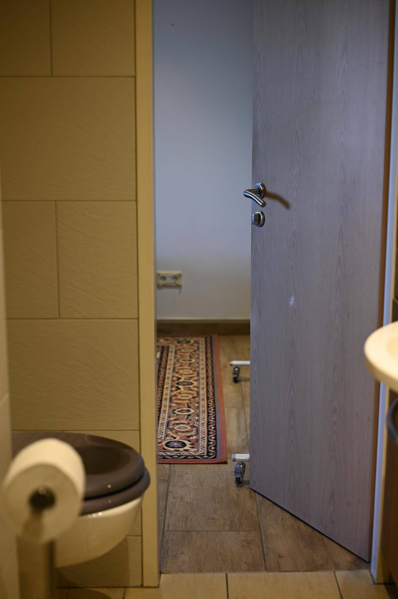 Separate Toilette mit Fliesenboden und Blick in einen angrenzenden Raum mit Teppich.