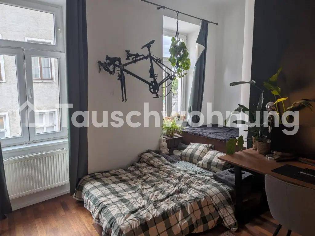 Schlafzimmer mit kariertem Bett, Wanddekoration und Schreibtisch am Fenster.