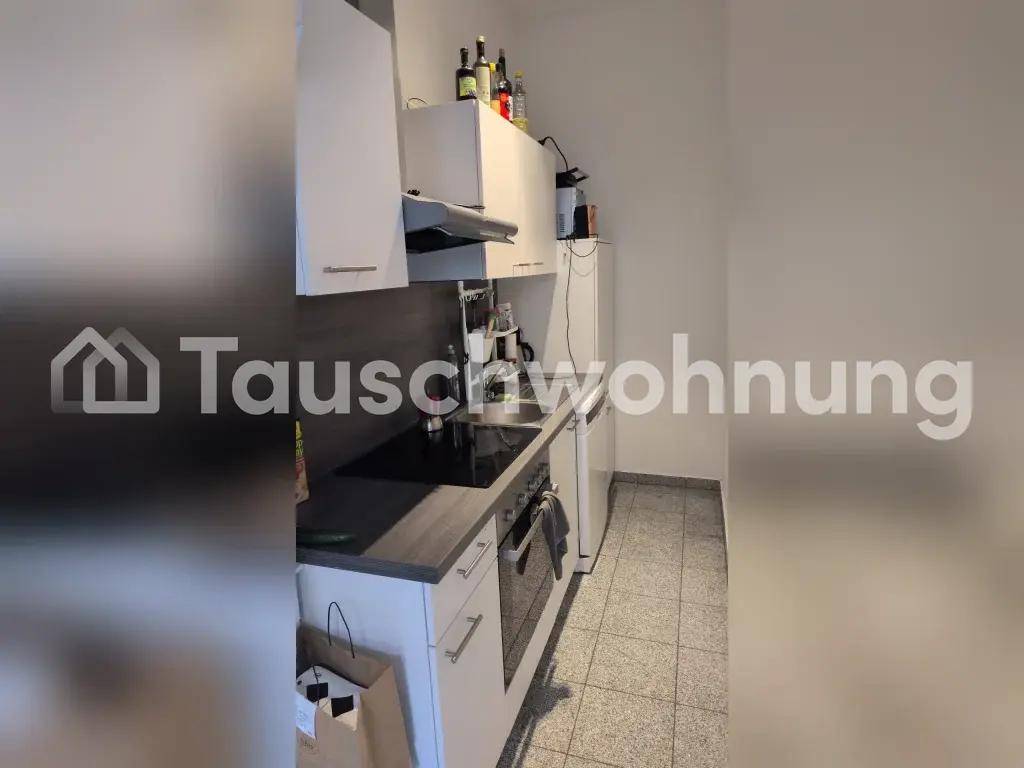 Kleine Küche mit weißen Schränken, integriertem Kochfeld und Fliesenboden.